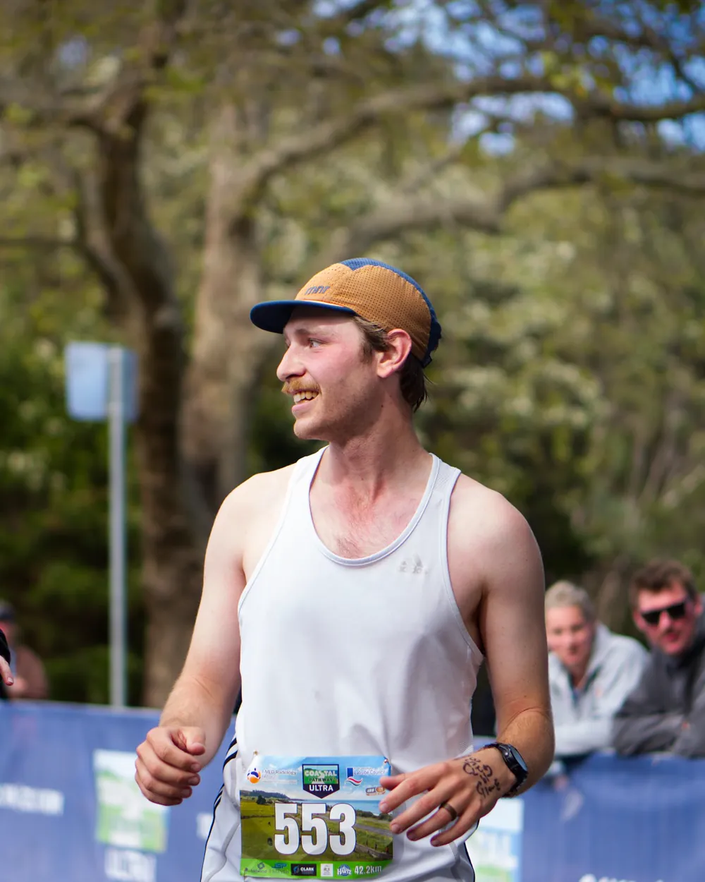 A smiling runner at the barrier beside the course, a supporter reaching towards him
